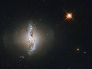 This Picture of the Week shows Arp 230, also known as IC 51, observed by the NASA/ESA Hubble Space Telescope. Arp 230 is a galaxy of an uncommon or peculiar shape, and is therefore part of the Atlas of Peculiar Galaxies produced by Halton Arp. Its irregular shape is thought to be the result of a violent collision with another galaxy sometime in the past. The collision could also be held responsible for the formation of the galaxy’s polar ring. The outer ring surrounding the galaxy consists of gas and stars and rotates over the poles of the galaxy. It is thought that the orbit of the smaller of the two galaxies that created Arp 230 was perpendicular to the disc of the second, larger galaxy when they collided. In the process of merging the smaller galaxy would have been ripped apart and may have formed the polar ring structure astronomers can observe today. Arp 230 is quite small for a lenticular galaxy, so the two original galaxies forming it must both have been smaller than the Milky Way. A version of this image was entered into the Hubble’s Hidden Treasures image processing competition by flickr user Det58. Links Atlas of Peculiar Galaxies